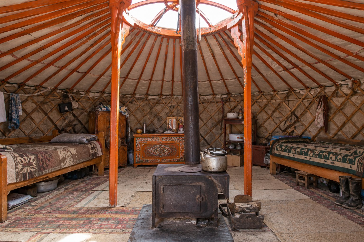 Intérieur d’une yourte mongole avec lits, charpente orange et poêle central